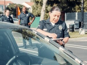 Can Police Search Your Car Without a Warrant in California? 2 Police officer writing a citation beside a vehicle while two officers stand in the background.